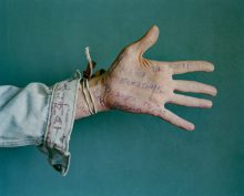 Syntolkad bildtext: En utsträckt hand och arm. På handen är det fullt med ord skrivet med kulspetspenna. Armen är klädd i jeansjacka som det också står ord på. 